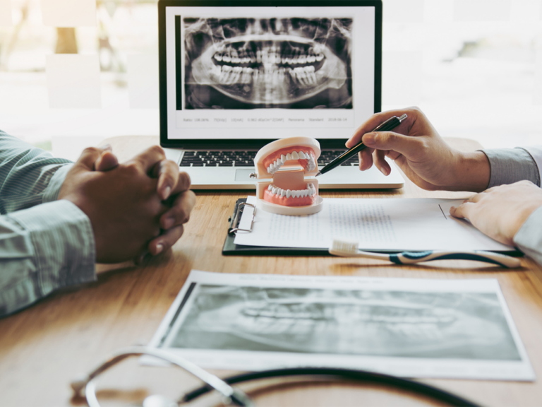 x-rays, paperwork, and a jaw model all on a desk in front of two men