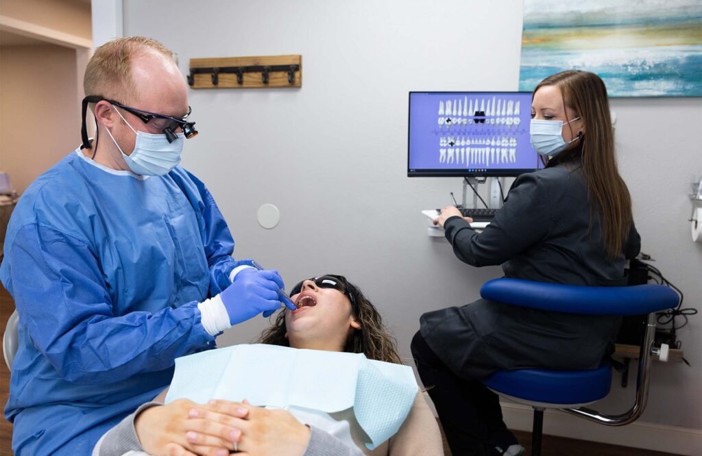 Dr. McKay cleaning a patient's teeth with an assistant watching on