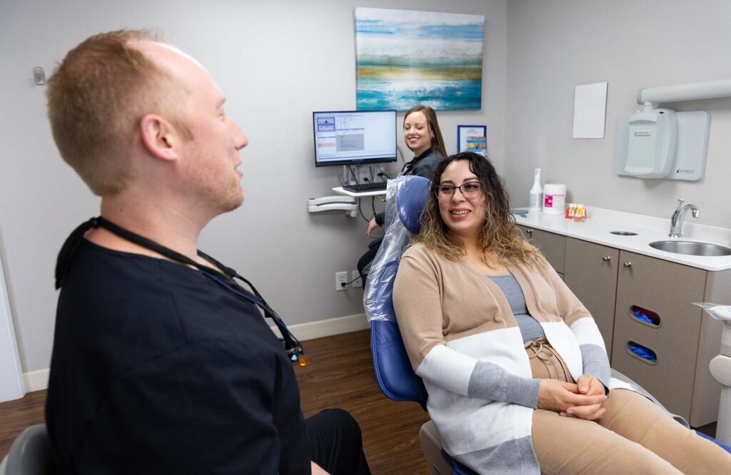 Dr. McKay talking to a smiling patient with an assistant smiling in the background